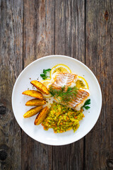 Fish dish - fried cod with baked potatoes and fresh vegetables on wooden table
