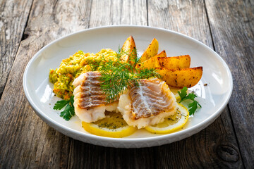 Fish dish - fried cod with baked potatoes and fresh vegetables on wooden table
