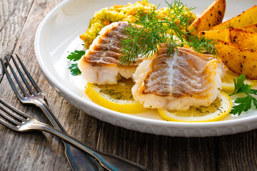 Fish dish - fried cod with baked potatoes and fresh vegetables on wooden table
