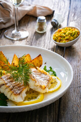 Fish dish - fried cod with baked potatoes and fresh vegetables on wooden table
