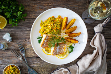 Fish dish - fried cod with baked potatoes and fresh vegetables on wooden table
