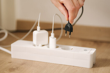 Human hand puts the charger into a filled extension cord. White cable connector. Close-up. Home...