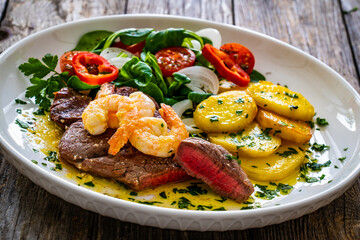 Fried beef sirloin steak with fried garlic prawns on and  potatoes on wooden table
