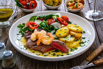Fried beef sirloin steak with fried garlic prawns on and  potatoes on wooden table
