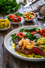Fried beef sirloin steak with fried garlic prawns on and  potatoes on wooden table
