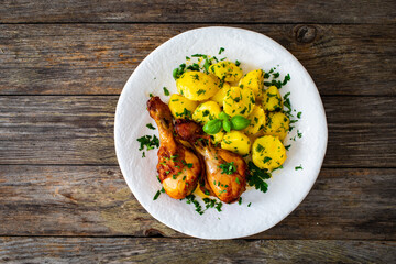 BBQ chicken drumsticks with fried potatoes, lettuce and ketchup on wooden table
