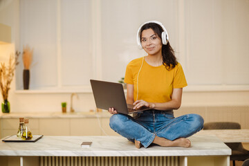 Portrait of indian or arabian woman inside home with headset for video call, woman smiling and looking at camera, couch customer support tech helpline.