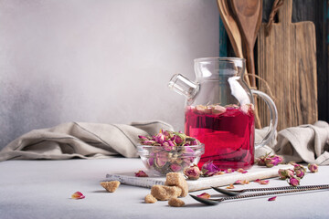 Glass teapot of sweet fragrant flower pink tea with dry rose buds and cane sugar