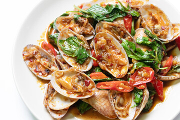 Stir-fried clams with chili paste and sweet basil on white plate. 