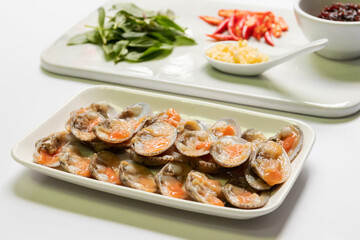 Fresh baby clams with red hot chili peppers, sweet basil leaves, chopped garlic in a spoon. Cooking ingredients for stir-fried clams with chili paste and sweet basil. 