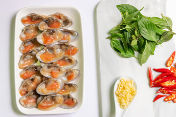 Fresh baby clams with red hot chili peppers, sweet basil leaves, chopped garlic in a spoon. Cooking ingredients for stir-fried clams with chili paste and sweet basil. 