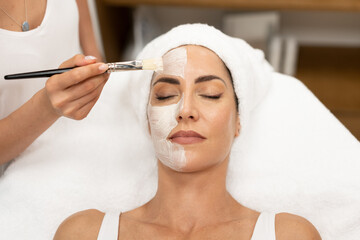Aesthetics applying a mask to the face of a Middle-aged woman in modern wellness center.