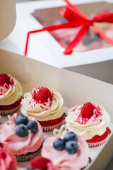 Fresh and delicious cupcakes with cheese cream and fresh berries. Top view of arranged tasty cupcakes in cardboard box isolated on white. Cakes with cream, chocolate bars, blueberries and raspberries 