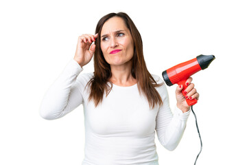 Middle age woman holding a hairdryer over isolated chroma key background having doubts and with confuse face expression