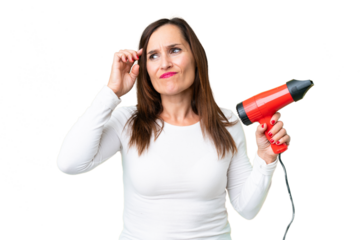 Middle age woman holding a hairdryer over isolated chroma key background having doubts and with confuse face expression