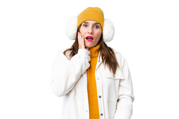 Middle age woman wearing winter muffs over isolated chroma key background surprised and shocked while looking right