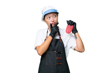 Young caucasian woman wearing an apron and serving fresh cut meat over isolated background having doubts
