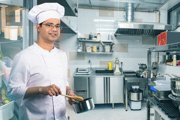 Man is cook. Restaurant kitchen employee with pan. Indian guy in chefs uniform. Cafe chef prepares...