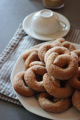 Italian homemade sweet cookies in shape of Taralli with coffee and powdered sugar on a white plate on gray table with Cappuccino cup 