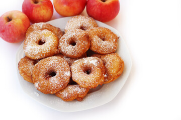 Homemade deep fried apple rings with batter sprinkled with powdered sugar on a plate isolated on white with fresh apples