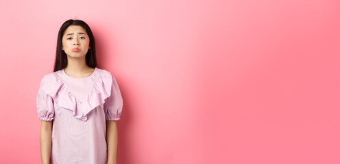 Sad whining asian girl pouting and frowning, looking upset about something unfair, complaining,...