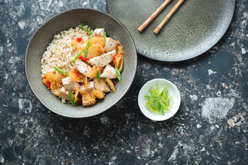 Bowl with korean chicken and kimchi stir-fry on a dark-brown granite background, horizontal shot, top view