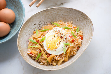 Kimchi fried rice served with chicken egg in a beige bowl, middle closeup, horizontal shot on a light-beige marble background