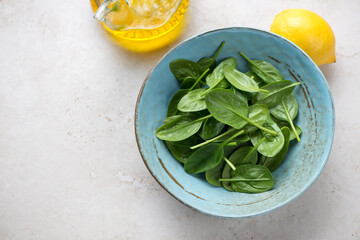 Turquoise bowl with fresh spinach leaves on a beige stone background, horizontal shot with space, elevated view