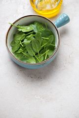 Turquoise bowl with fresh spinach salad, vertical shot on a beige stone background, high angle view, copy space
