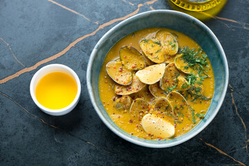 Bowl of chickpea cream-soup with littleneck clams and greens on a dark-olive marble background, high angle view, horizontal shot