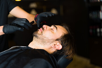 Young man relaxing while getting a beard shave a the barber shop