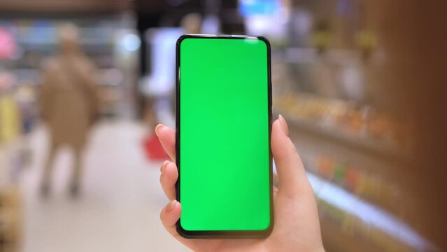 4k Mobile phone Chroma key for mobile app application. Close up of woman hand holds smart phone with green screen at shopping mall store. Buying food at supermarket, grocery shop center online