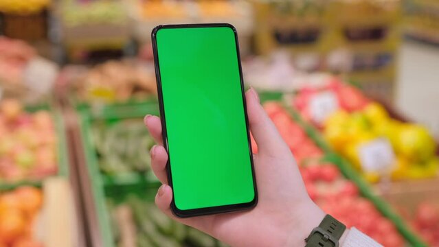 4k Mobile phone Chroma key for mobile app application. Close up of woman hand holds smart phone with green screen at shopping mall store. Buying food at supermarket, grocery shop center online