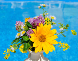 Bright colorful bouquet of wild flowers in a clay vase against the backdrop of a blue pool.