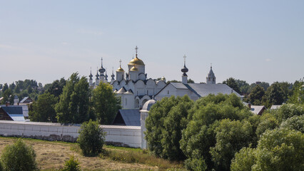 The ancient white-stone Pokrovsky convent in the historical place of Suzdal, Vladimir region, on a sunny summer day among green trees and a space for copying