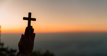 Silhouette of young woman kneeling down praying and holding christian cross for worshipping God at...