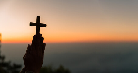 Silhouette of young woman kneeling down praying and holding christian cross for worshipping God at sunset background. concept of christian kneeling and praying to god.