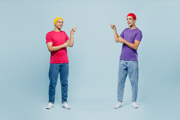 Full body smiling cheerful cool young couple two friends men wear casual clothes together point index fingers on area between them isolated on pastel plain light blue cyan background studio portrait.