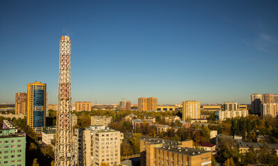 A beautiful urban landscape with tall modern houses and a metal pipe of a thermal power plant against the background of a clear blue sky on an autumn day