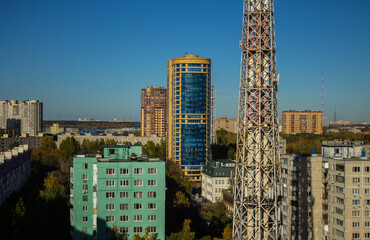 A beautiful urban landscape with tall modern houses and a metal pipe of a thermal power plant against the background of a clear blue sky on an autumn day