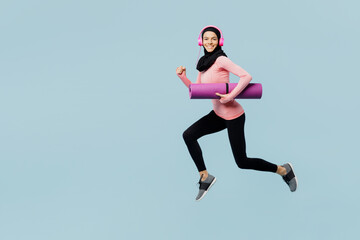 Full body young asian muslim fitness trainer sporty woman wear pink abaya hijab headphones hold yoga mat spend time in home gym isolated on plain blue background studio. Workout sport fit abs concept.