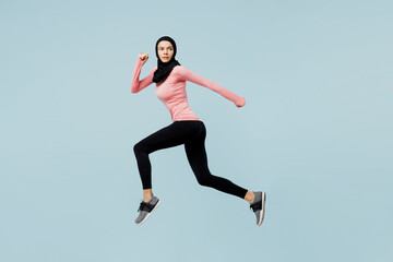 Fototapeta na wymiar Full body sideways young asian muslim fitness trainer sporty woman wear pink abaya hijab spend time in gym run fast jump high isolated on plain blue background studio. Workout sport fit abs concept.