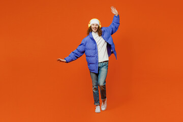 Young man with long curly hair wearing hat purple ski padded jacket casual clothes headphones listen to music dance raise up hands close eyes isolated on plain orange red background studio portrait.