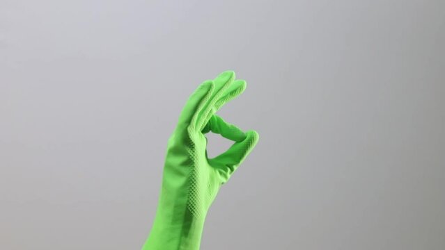 Cleaners hand in green rubber glove showing OK gesture with fingers, hand, closeup.
