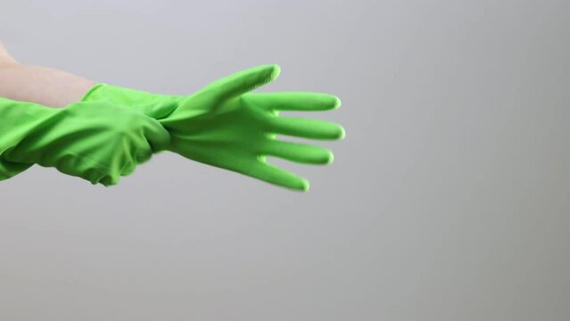 Female cleaners hands putting on green rubber gloves closeup on gray background.