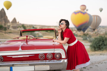 beautiful girl in retro style posing near a vintage red cabriolet car on background of balloons in Cappadocia.