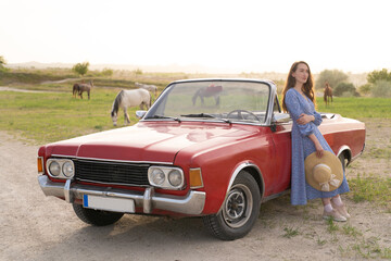 beautiful girl in retro style posing near vintage red cabriolet car.