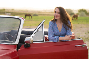 beautiful girl in retro style posing near vintage red cabriolet car.