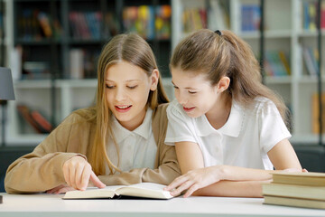 School children sitting at desk together, reading funny book and laughing, friends having fun in class. Pupils studying in class. Concept of education