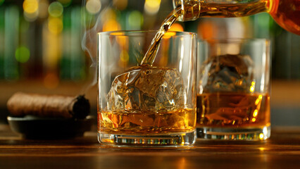 Detail of pouring whiskey into glass with ice cubes.